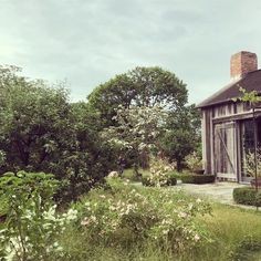 an old house surrounded by greenery and flowers in the foreground, with a small garden behind it