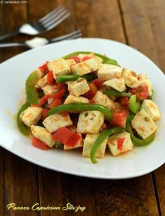 a white plate topped with tofu and green peppers on top of a wooden table