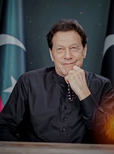 a man sitting at a table in front of flags with his hand on his chin