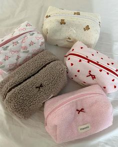 four small purses are lined up on a white sheet, one has a cross and the other has hearts