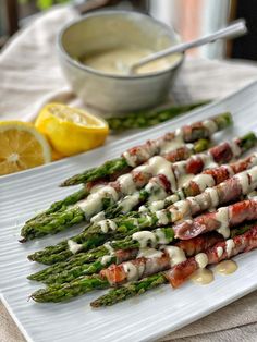 asparagus wrapped in bacon and sauce on a white plate with lemon wedges