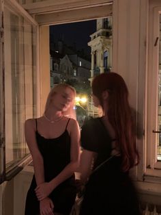 two beautiful young women standing next to each other in front of a window at night