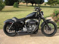 a black motorcycle parked on top of a dirt road next to a lush green field