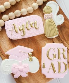 decorated cookies on a wooden tray with beads and necklaces around them that say, ayea, grad, graduation