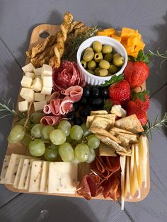 an assortment of cheeses, fruits and meats on a wooden platter with olives