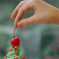 a hand holding a cherry on top of a cupcake with sprinkles