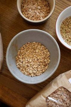 three bowls filled with oatmeal sitting on top of a wooden table next to two bags