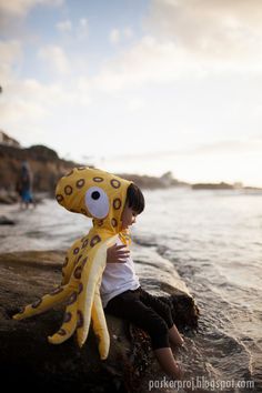 a little boy sitting on the rocks with a stuffed animal in front of his face