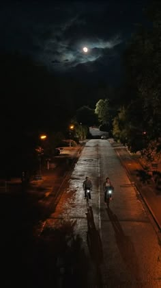 two bicyclists are riding down the road at night with full moon in background