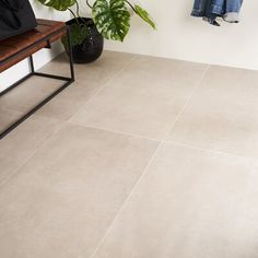 a bench sitting next to a potted plant on top of a tiled floor in front of a white wall