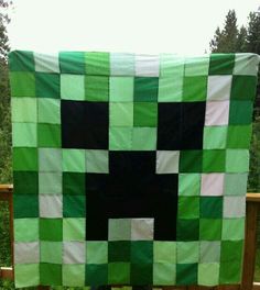 a man is holding up a green and black quilt that looks like a square shape