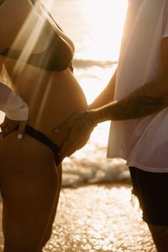 a man and woman standing next to each other in front of the ocean at sunset