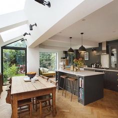 an open kitchen and dining area with wooden floors, large windows, and skylights