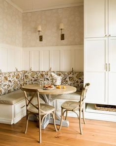 a corner table with two chairs and a bench in the middle of a room filled with white cupboards