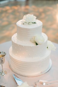 a white wedding cake sitting on top of a table next to two silver spoons