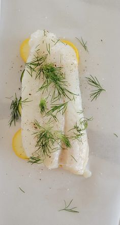 some kind of fish on a white plate with lemon wedges and dill garnish