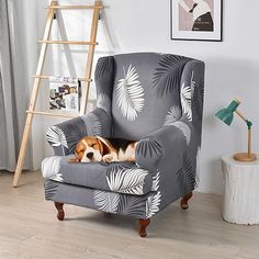 a dog laying in a grey chair with palm leaves on it's armrests