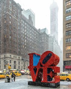 a large red love sculpture sitting in the middle of a snow covered street next to tall buildings