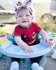 a baby sitting in a booster seat with a bow on it's head and smiling