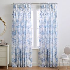 a white and blue floral curtain hanging in front of a window next to a dresser