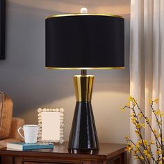 a table lamp with a black shade on it next to a coffee cup and vase