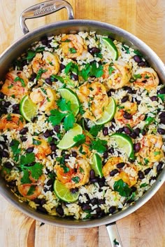 a skillet filled with rice, black beans and limes on top of a wooden table