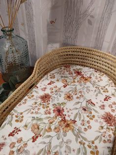 a wicker crib with a floral print on it and a vase next to it