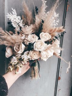 a person holding a bouquet of flowers in front of a wooden door with dried grass