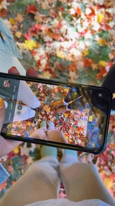 a person taking a photo with their cell phone in front of an autumn scene and falling leaves