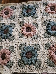 a crocheted granny blanket with flowers on the front and center, sitting on top of a wooden table