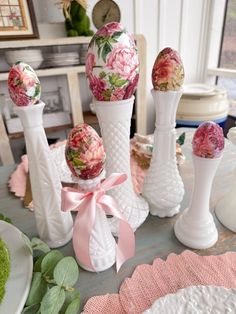 some white vases with flowers and eggs in them sitting on a dining room table