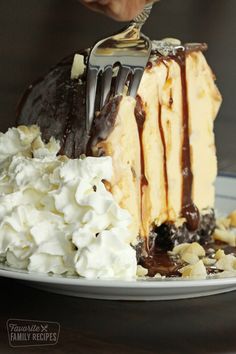 someone is cutting into a piece of cake on a plate with whipped cream and chocolate sauce