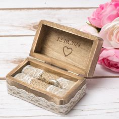 an open wooden box with a wedding ring in it and flowers on the table next to it