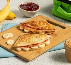 two quesadillas on a cutting board with peanut butter and bananas next to them