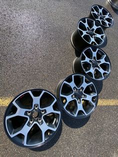 four black rims are lined up next to each other on the pavement in front of a yellow line