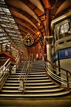 an escalator in a train station with stairs leading up to the clock tower