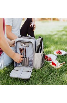 a person sitting in the grass with an open backpack and utensils on it