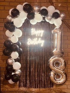 a birthday decoration with balloons and streamers in front of a brick wall that says happy birthday