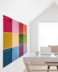 a laptop computer sitting on top of a white desk next to a wall mounted calendar