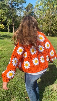 the back of a woman's orange sweater with white daisies and yellow centers