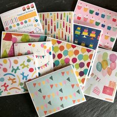 many different cards and envelopes are arranged on a black surface, including one with balloons