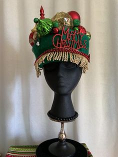 Christmas party in your future? This exotic vintage green wool hat loaded with shatter resistant bulbs in reds, greens and golds. Gold fringe circles the front of the hat. "Merry Christmas" in glitter letters is above the fringe. a piece of silk mistletoe calls out if you're looking for a kiss or two. (There are a couple of breakable twist ornaments. They add a great look, but are very delicate. I include a few glitter balls to be glued onto any ends if they break.) All of my offerings are made Diy Christmas Hats, Christmas Hats, Holiday Hats, Gold Fringe, Sweater Hat, Christmas Tops, Glitter Letters, Button Art, Red Button