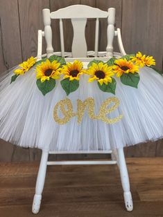 a white chair with sunflowers and the word one on it in gold glitter