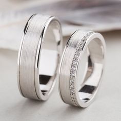 two white gold wedding rings with diamonds on top of each other, sitting next to each other