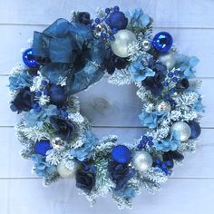 a wreath with blue and silver ornaments hanging on a white wooden wall in front of a door