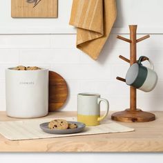 two mugs and a cookie on a wooden table next to a tea towel rack