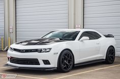 a white chevrolet camaro is parked in front of some garage doors