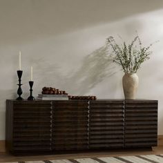 a vase with some plants on top of it next to a wooden sideboard in a room