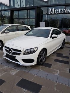 two white cars parked in front of a mercedes dealership