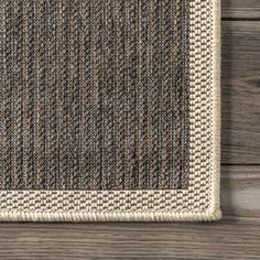 an area rug on top of a wooden floor with a white border and brown trim